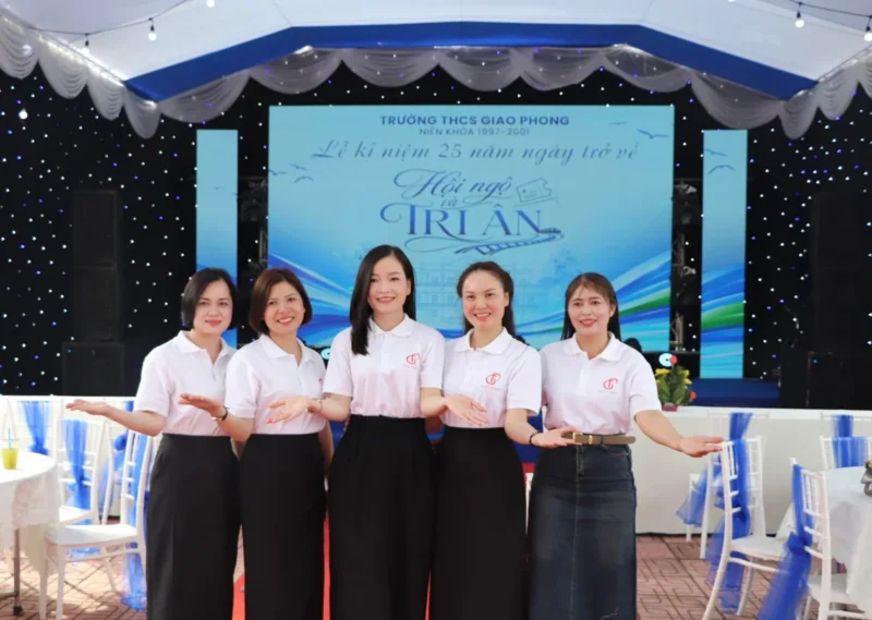 Áo kỷ niệm 25 năm ra trường THCS Giao Phong – Nhóm khách hàng mặc áo đồng phục, chụp ảnh cùng bảng kỷ niệm tại sân khấu. – 5