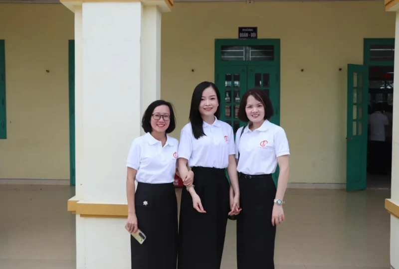Áo kỷ niệm 25 năm ra trường THCS Giao Phong – Ba cựu học sinh mặc áo polo trắng có logo GP trước lớp học. – 6
