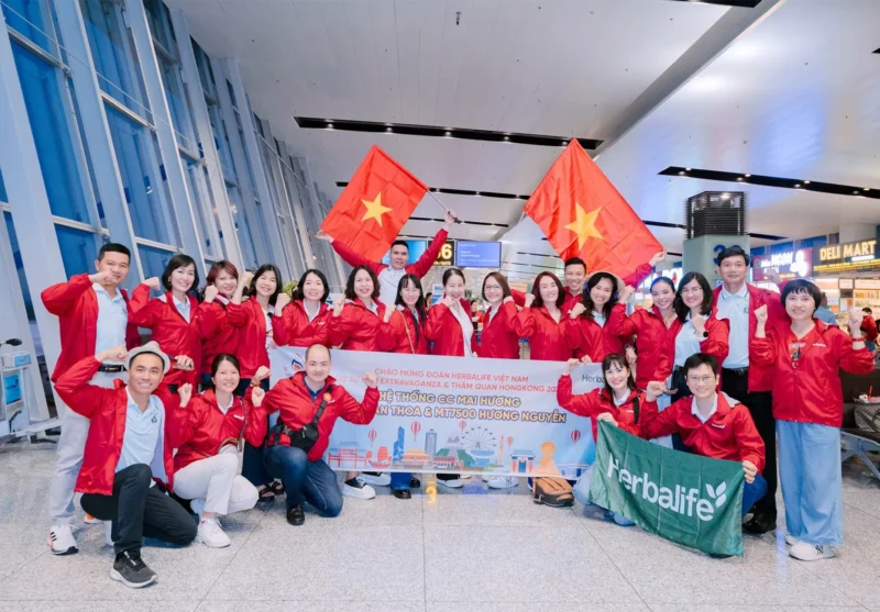 Nhóm khách hàng mặc áo khoác gió đỏ tại khu vực sân bay trong chuyến tham gia sự kiện.