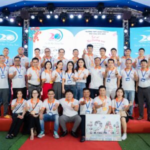 Nhóm cựu học sinh K29 THPT Giao Thủy B chụp ảnh trong áo polo trắng phối cam trước sân khấu hội khóa.